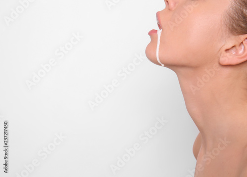 Young woman with white liquid dripping from her mouth on light background. Erotic concept