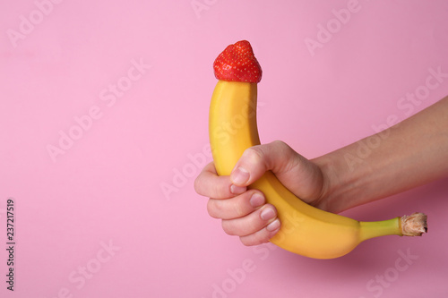 Woman holding banana with strawberry on color background. Erotic concept