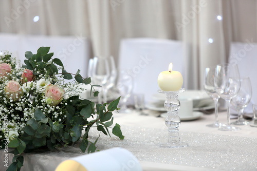 Biała świeca i bukiet kwiatów na białym stole.