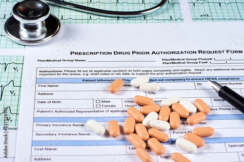 Prescription drugs prior authorization request form, pills, stethoscope and pen on a EKG graph paper background. Close-up.