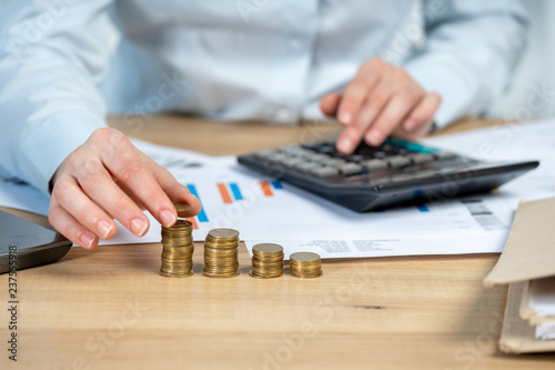 Close up cropped investor or sale manager lady in her formal wear shirt she put money in pile sit behind table in bright loft interior workstation count tax on invoice focus on hand with coins