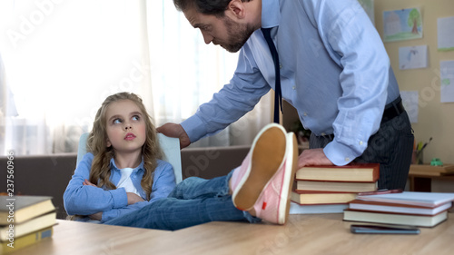 Mischievous daughter sitting with legs on table, ignoring fathers remarks