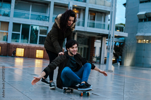 Teenage couple has fun with the skateboard in a modern city square