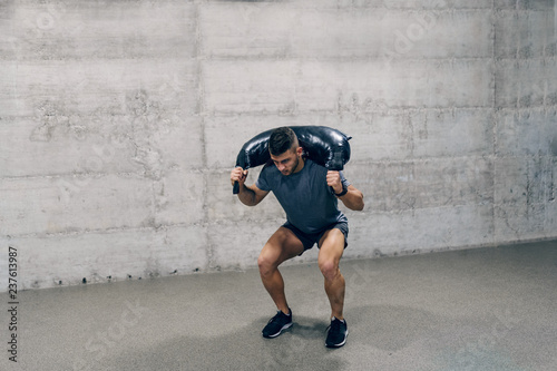 Strong Caucasian sporty man in sportswear lifting Bulgarian training bag. Don't stop until you are proud.