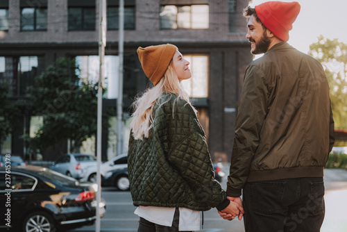 Side view portrait of charming girl in hat spending time with her boyfriend outdoors. They looking at each other with love and smiling