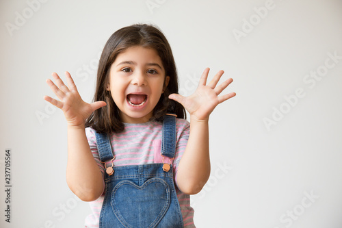 Excited preschooler child screaming and showing palms. Cute joyful Hispanic kid with funny grimace. Isolated on white with copy space. Having fun concept