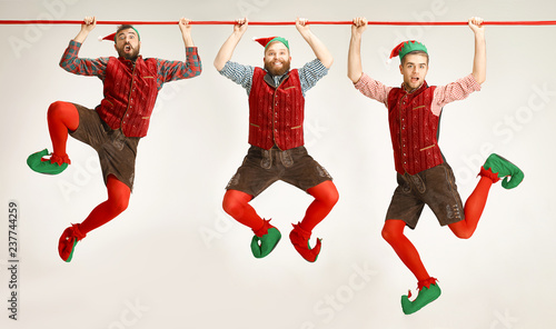 The happy smiling friendly men dressed like a funny gnome or elf hanging on an isolated gray studio background. The winter, holiday, christmas concept