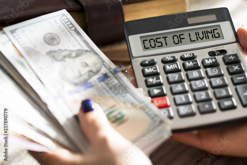 Woman calculating cost of living with calculator cash us dollar banknotes