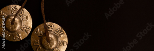 Tingsha Cymbals Tibetan Buddhist Lucky Symbol Embossed Meditation Yoga Bell Chimes on black contrasting background. Tibetan bells for singing mantra. Header for a site about meditation.