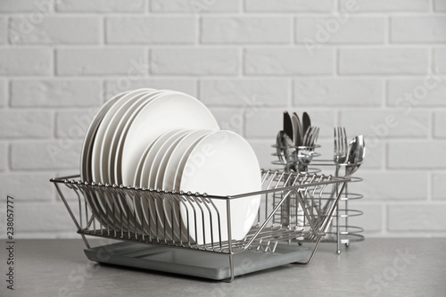 Dish rack with clean plates on table near brick wall