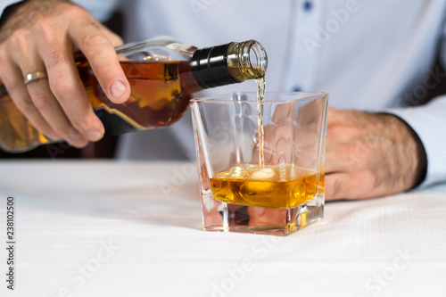 Męska dłoń nalewa whisky z butelki do szklanki z lodem.