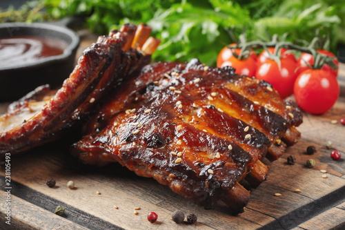 Closeup of pork ribs grilled with BBQ sauce and caramelized in honey. Tasty snack to beer on a wooden Board for filing on dark concrete background