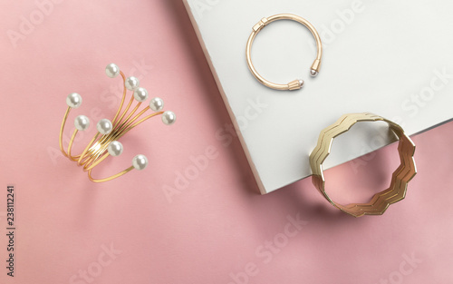 Golden bracelet with pearls and golden zigzag shape cuff on pink and white paper background