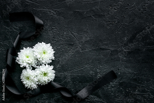 Funeral symbols. White flower near black ribbon on black background top view space for text