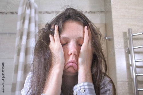 Woken tired woman in the bathroom with hangover and headache.