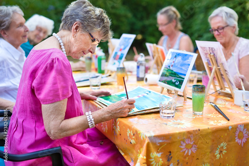 Senior lady painting in art class with friends.