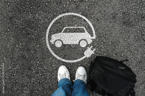 a man with a shoes is standing next to electric car sign on road asphalt