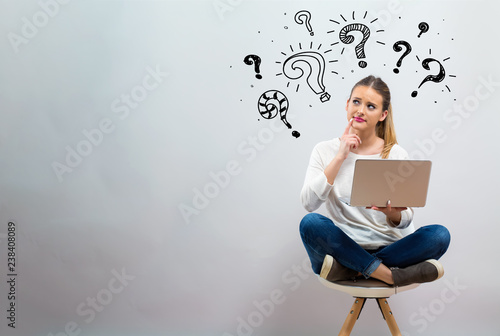 Question marks with young woman using her laptop on a grey background