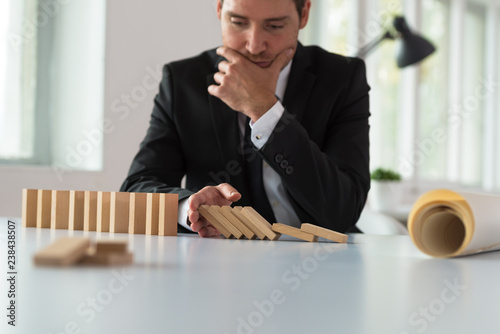 Worried serious businessman sitting at his desk stopping domino effect