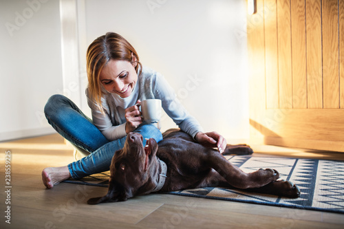 A young woman sitting indoors on the floor at home, playing with a dog.