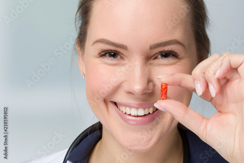 Eine junge lächelnde Frau hält eine Tabletenkapsel in der Hand