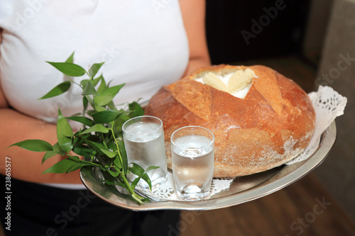 Kelnerka trzyma bochenek chleba z solą, wodą i wódką na przywitanie młodej pary. 