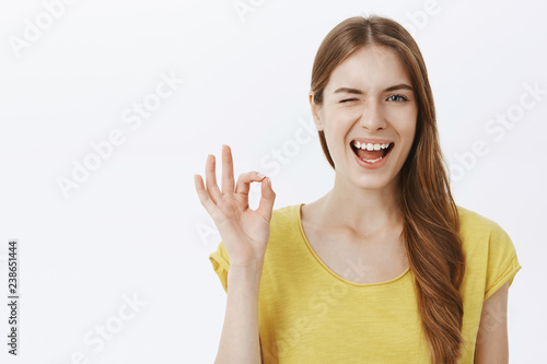 I got everything under control. Portrait of pleased confident and energized good-looking female in yellow casual t-shirt winking and smiling broadly showing okay gesture confirming and approving plan