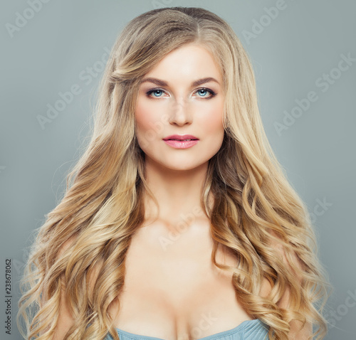 Gorgeous blonde woman with long healthy curly hair and clear skin. Facial treatment, haircare and cosmetology