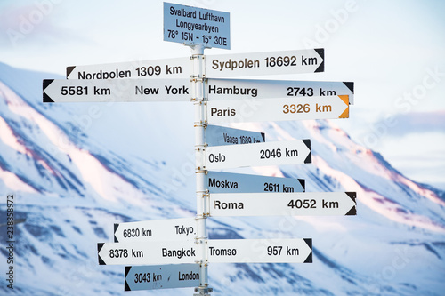 Big pole with directions signs and distances to cities of the world. Blue sky, mountains covered with snow. Longyearbyen, Spitsbergen, Norway