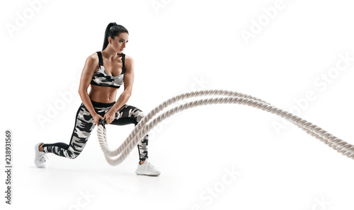 Muscular woman working out with heavy ropes. Photo of sporty woman in military sportswear isolated on white background. Strength and motivation. Side view