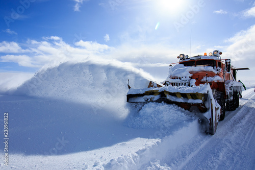 Snow plowing truck, huge heavy machine service car, snow flakes and splash off road, winter cold snowy season, snow cleaning, sunny blue sky day at cold Russian arctic north, industrial view