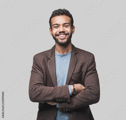 Portrait of handsome smiling young man with folded arms. Laughing joyful cheerful men with crossed hands studio shot. Isolated on gray background