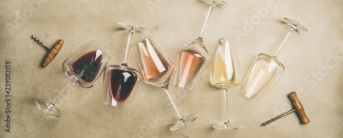 Flat-lay of red, rose and white wine in glasses and corkscrews over grey concrete background, top view, wide composition. Wine bar, winery, wine degustation concept