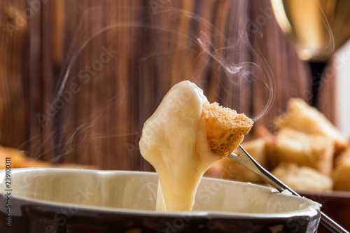 Close up, macro. Traditional french cheese fondue. Crouton dipped into stemy-hot cheese fondue on a long-stemmed fork. Copy space.