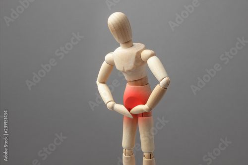 Concept pain in the groin, problems with the genitals. The wooden man holds his hands over the groin area in red