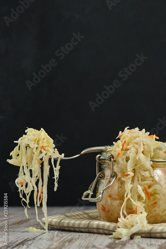 one jar of sauerkraut and carrots in its own juice with spices on a light, white wooden table, black background, horizontal view of the cabbage in the jar. traditional home-made, 