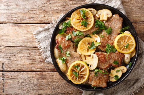 Tasty Italian fillet of veal scaloppini with mushrooms and lemons in sauce close-up in a frying pan. Horizontal top view
