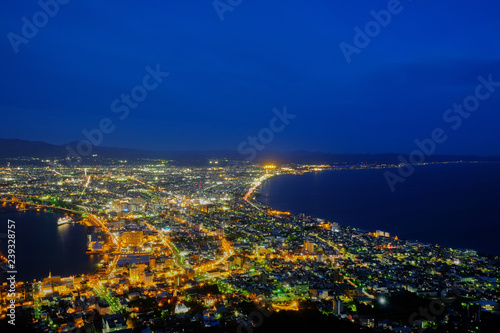take a look city and harbor view point after sunset, see blue sky and light house at Mount Hakodate, Hokkaido, japan