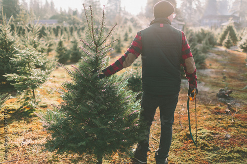 A man at a Christmas tree farm standing with the tree he cut down. 