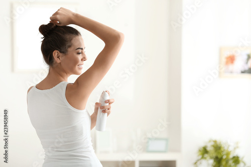 Young woman using deodorant at home