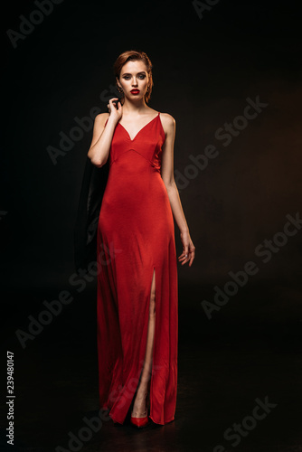 attractive girl in red dress holding black jacket and walking isolated on black