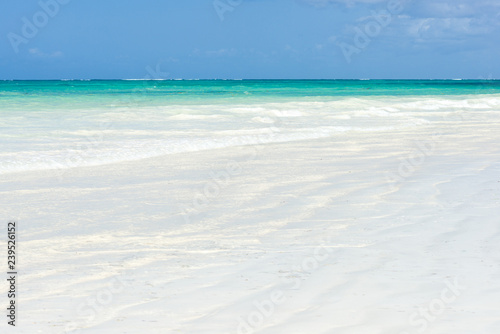 Tropical beach view with waves gently break on the shoreline on a sunny day, Diani, Kenya