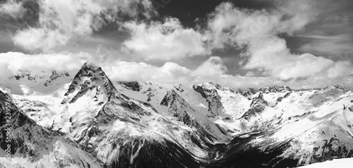 Black and white panorama of snowy winter mountain in sunlight clouds