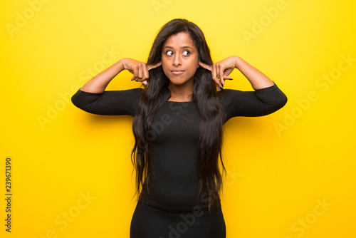 Young afro american woman on vibrant yellow background covering both ears with hands