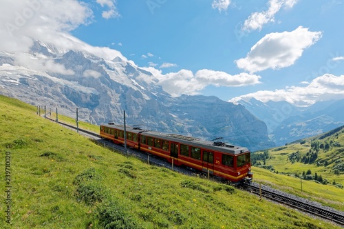 July, 6, 2018, A cog wheel train travels on famous Jungfrau Railway from Kleine Scheidegg to Jungfraujoch station ( top of Europe ) on a green grassy hillside, in Berner Oberland, Switzerland 