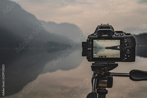 Camera on tripod at work on a misty lakeshore. Camera display. Taking pictures using the display.