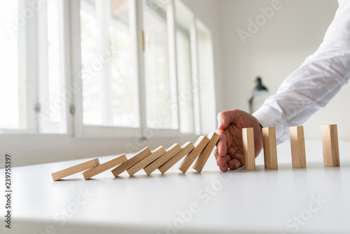 Hand of a business advisor stooping domino effect