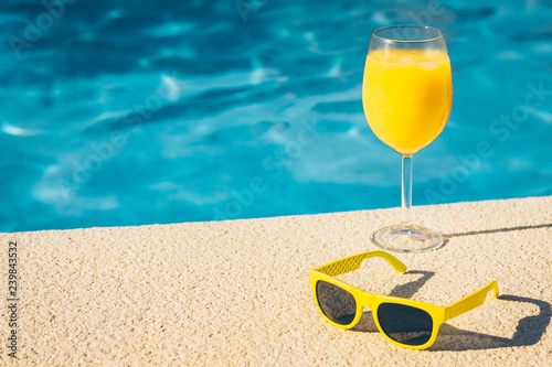 Transparent glass with a refreshing drink - an alcoholic cocktail or smoothie and yellow trendy glasses on the edge of the pool - copy space