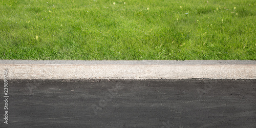 Green Grass Grows Near Black Asphalt, Separated By Concrete Border. Road And Lawn Divided By Concrete Curb.