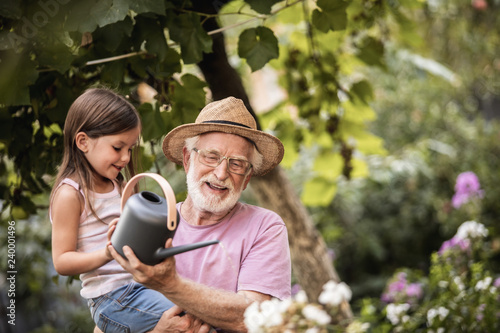 Little girl helping her grandpa watering plants